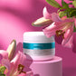 A jar of Freedom Moisturizer on pink pedestal with pink flowers on the bottom left and right of it.